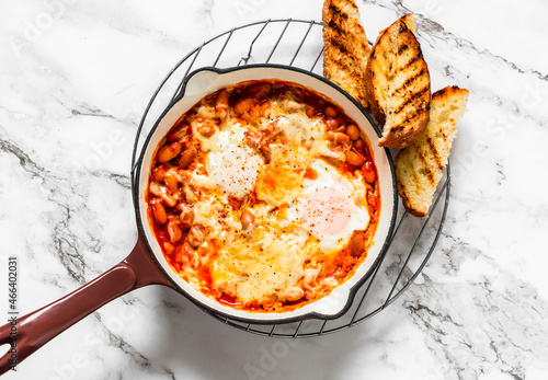 Tomato sauce beans, cheese, eggs baked shakshuka in a ceramic frying pan with a grill crispy bread on a light background, top view photo