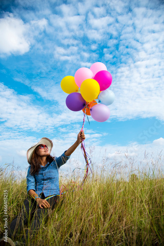 Woman holding balloons running on green meadow white cloud and blue sky with happiness Cheerful and relax. Hands holding vibrant air balloons play on birthday party happy times summer sunlight outdoor