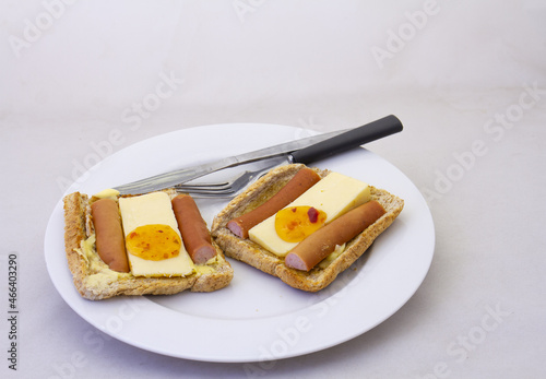 Slices of toast with cheese, sausage and chutney on a white plate with eating utensils