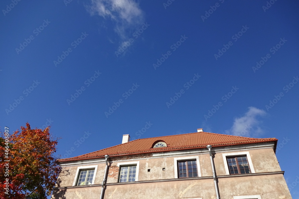 Close up of a house with red tiled roof. Cear blue sky background. Golden autumn tree foliage on the left. Autumn mood. Pelgulinna, Tallinn, Estonia, Europe. September 2021