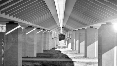 Sunlight penetrates under overpass. Highway overpass bridge concrete structure with columns. Black and white.