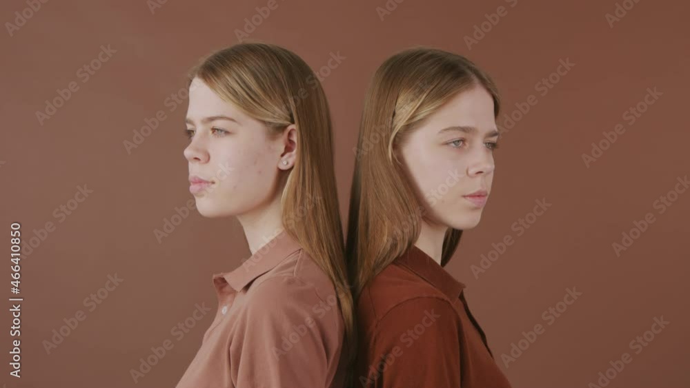 PAN shot of identical twin sisters standing back to back isolated on brown background PAN shot of identical twin sisters standing back to back isolated on brown background