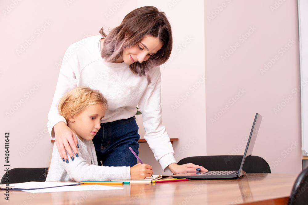 Young female teacher teaches a cute girl child schoolgirl in the classroom at the table using a laptop Young female teacher teaches a cute girl child schoolgirl in the classroom at the table using a laptop