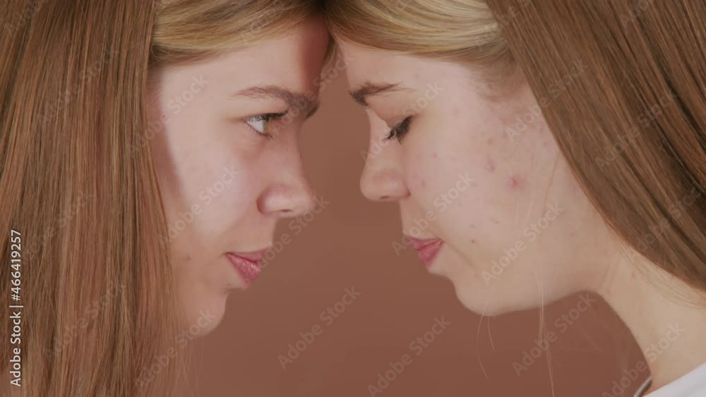 Extreme close up shot of happy twin sisters touching foreheads and smiling while looking at each other and posing isolated on brown background Extreme close up shot of happy twin sisters touching foreheads and smiling while looking at each other and posing isolated on brown background