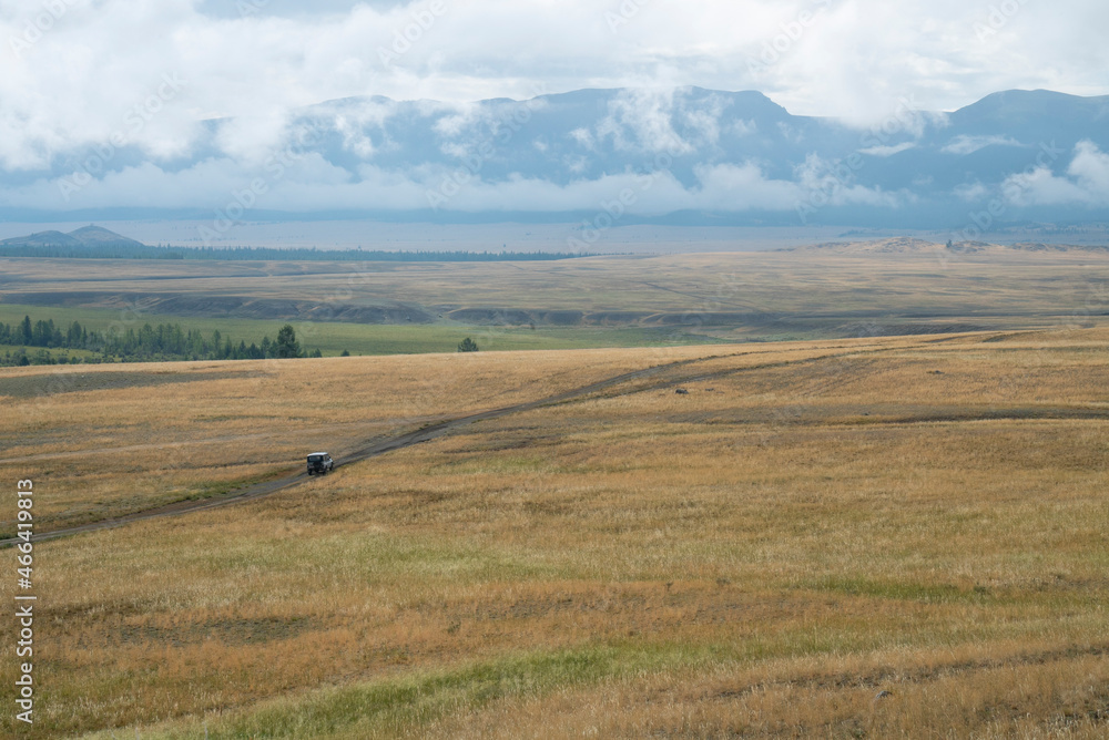 An SUV rides across the steppe against the backdrop of mountains