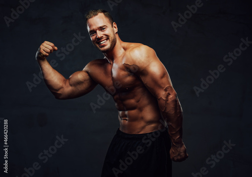 Guy with naked torso and huge biceps posing in studio