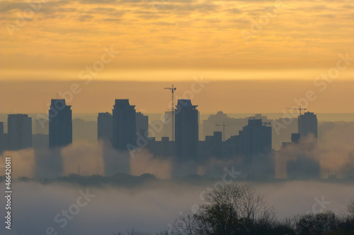 Foggy view of the morning city. Fiery dawn in Kiev. Buildings in the fog