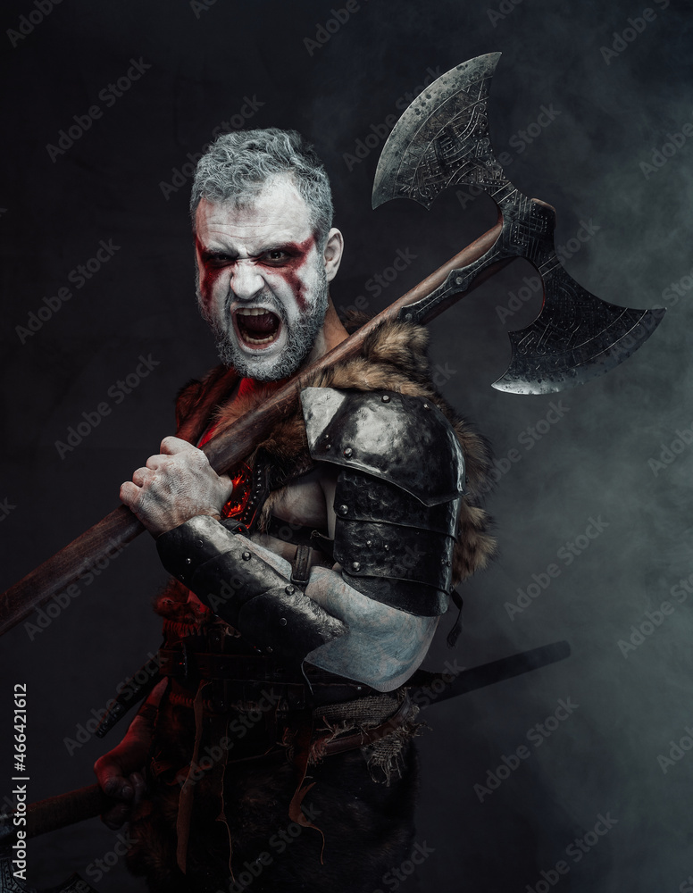 Naklejka premium Screaming mythical warrior with painted skin and axe in studio