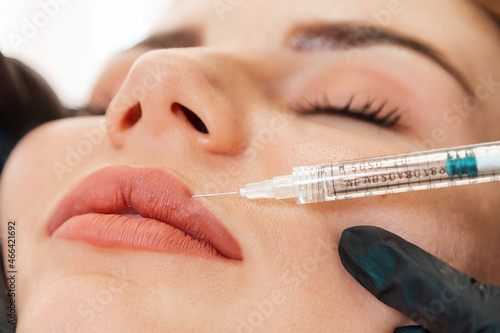 Aesthetic medicine and cosmetology. Cosmetologist in black latex gloves makes with syringe injects of a medical in lips. Close up of face. Concept of plastic surgery