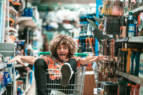 An afro teenager with a crazy face is sitting in a trolley in a big shopping mall. Fun shopping