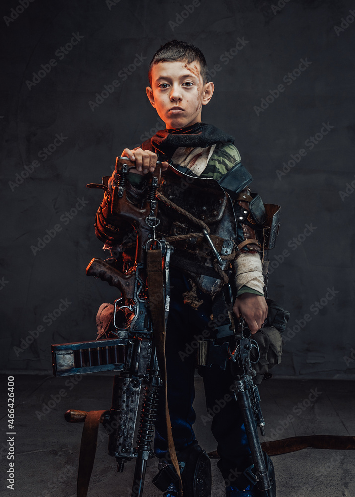 Naklejka premium Young boy in ragged clothing with shotgun in dark background