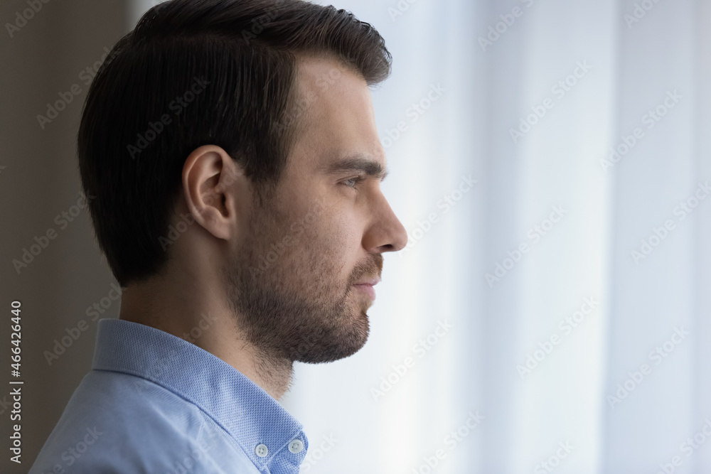 Close up head shot side view dreamy confident young handsome man looking in distance out of window, visualizing successful future, planning weekend or vacation trip, meditating alone at home. Close up head shot side view dreamy confident young handsome man looking in distance out of window, visualizing successful future, planning weekend or vacation trip, meditating alone at home.
