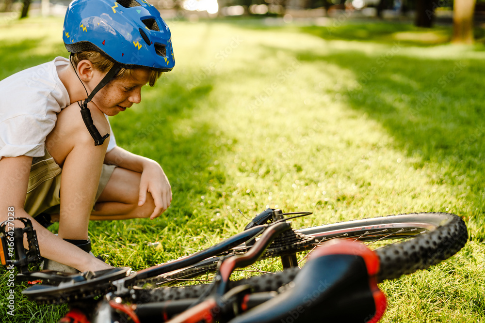 Naklejka premium Ginger white boy wearing helmet smiling while squatting by his bicycle