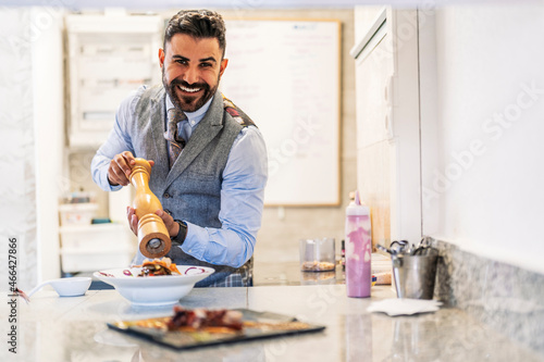 Smiling male chef with pepper grinder at kitchen counter photo