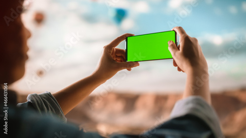 Close Up of Multiethnic Traveller with Curly Hairstyle Taking a Smartphone Photo on a Phone with Green Screen Display of the Rocky Canyon Valley. Hot Air Balloon Festival in Mountain National Park.