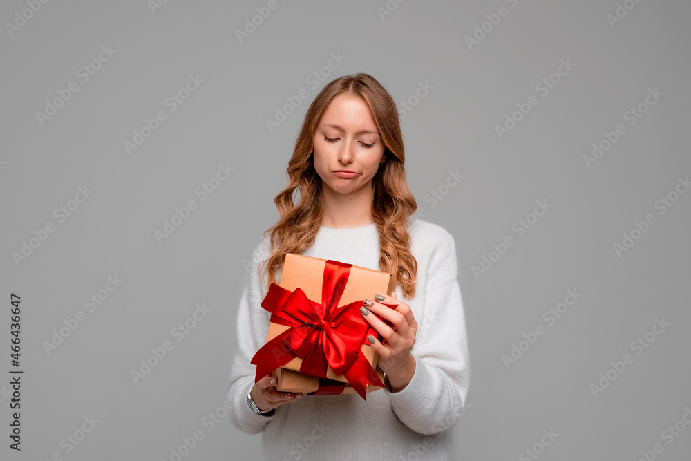 Young woman in white sweater opening birthday gift on party celebration, looking disappointed unhappy, standing over gray background. Holidays, celebration and lifestyle concept Young woman in white sweater opening birthday gift on party celebration, looking disappointed unhappy, standing over gray background. Holidays, celebration and lifestyle concept