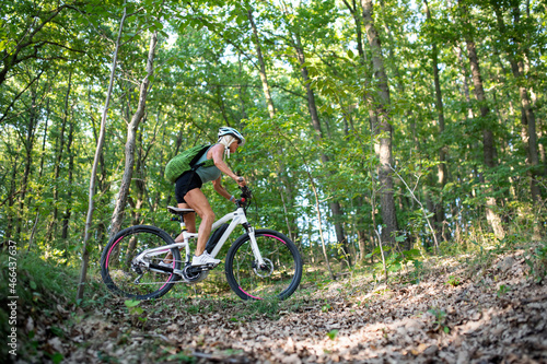 Low angle view of active senior woman biker cycling outdoors in forest. © Halfpoint