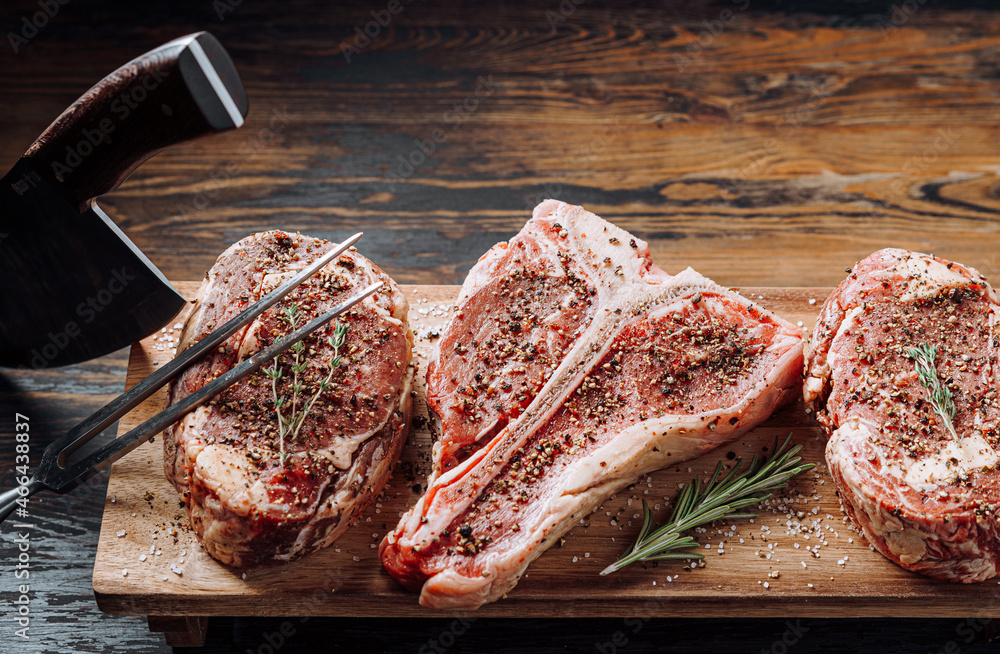 three lovely raw marbled black Angus beef steaks flavored with a mixture of ground pepper and ready to cook and serve on a dark wooden background.