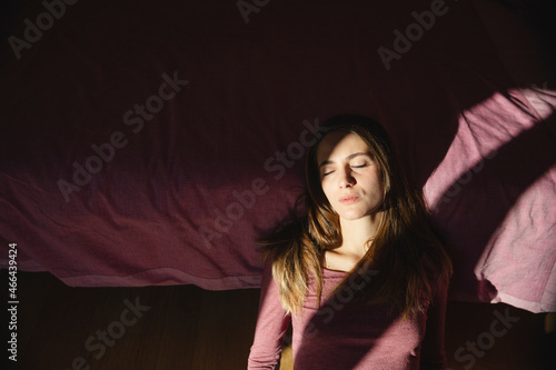 Young depressed woman with eyes closed leaning on bed at home photo