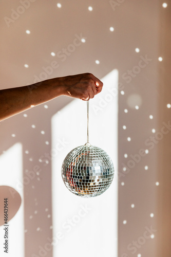 Young woman holding shiny disco ball in front of wall at home