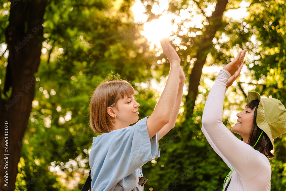 Multiracial two women smiling and giving high five while walking in park