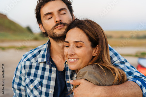 White couple smiling and hugging while standing by their car