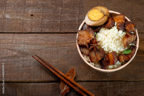Bowl with rice and braised pork belly on a wooden background, free space, top view.