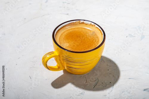 Yellow mug with fresh coffee on a beige textured background, hard light, free space.