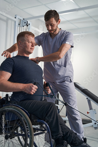 Doctor examining wheelchair patient shoulder pain. Checking posture