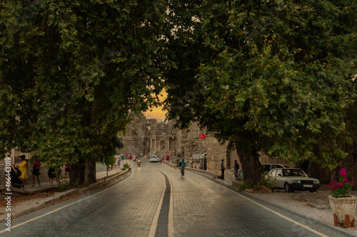 Views of the stone paved road leading from the entrance gate of the ancient city of Side towards the city center. Cloudy Sunset Sky and Sea view. Dust, Dark and Shadow
