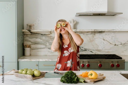 Happy female nutritionist covering eyes with avocado in kitchen photo