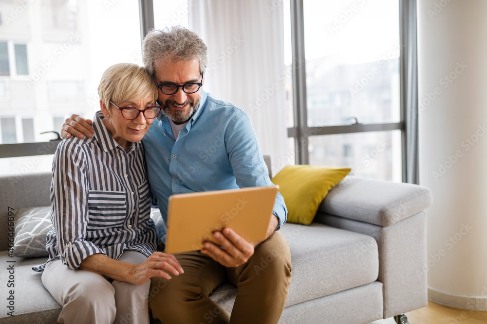 Beautiful happy mature couple is using a digital tablet, talking and smiling at home Beautiful happy mature couple is using a digital tablet, talking and smiling at home