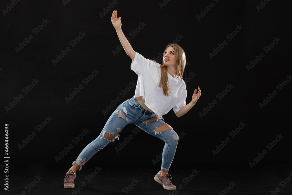 A teenage girl is performing a pose from a dance routine while standing wide apart, facing the camera. Long blonde hair.