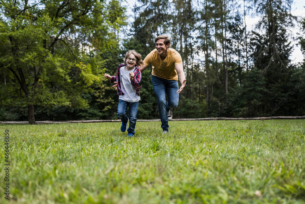 Playful son and father running on grass at park Playful son and father running on grass at park