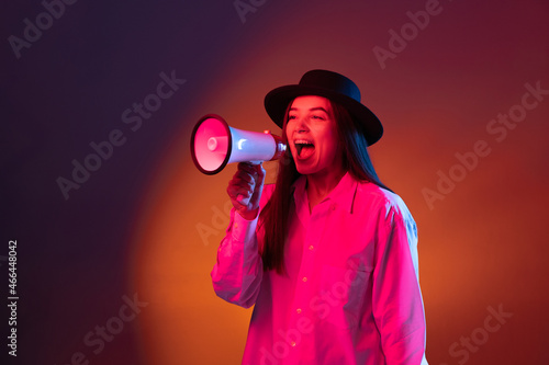 Emotional young girl shouting at megaphone isolated on dark studio background in neon light.
