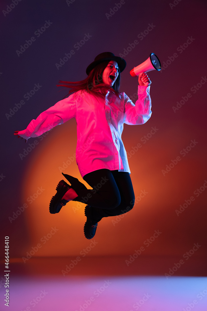 Emotional young girl shouting at megaphone isolated on dark studio background in neon light.