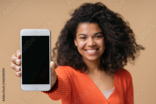 Smiling curly haired African American woman showing mobile phone screen isolated on background, selective focus. Copy space