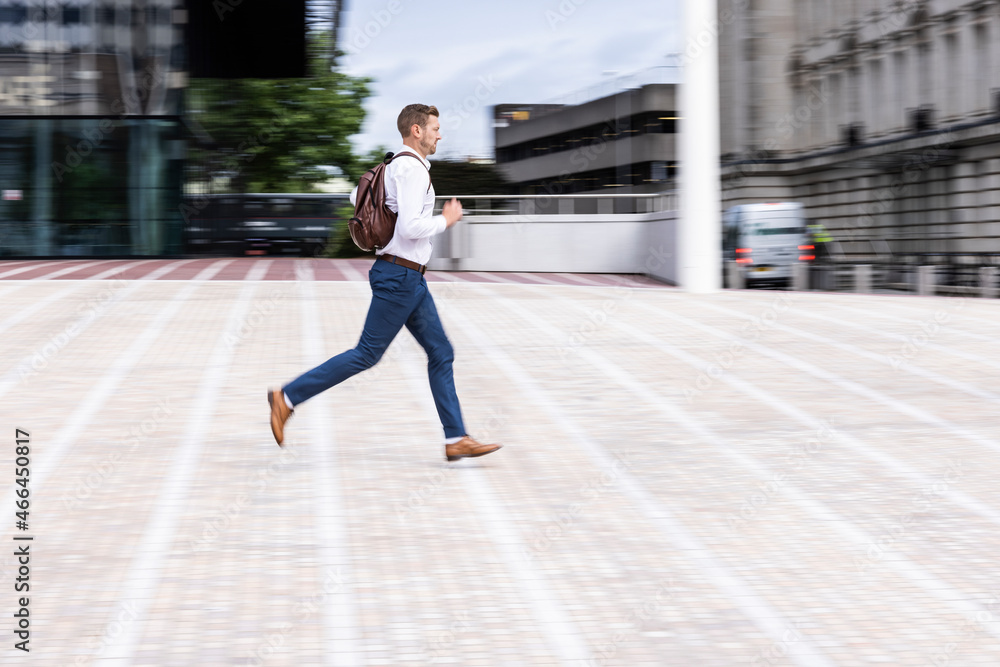 Businessman wearing backpack while running on footpath Businessman wearing backpack while running on footpath