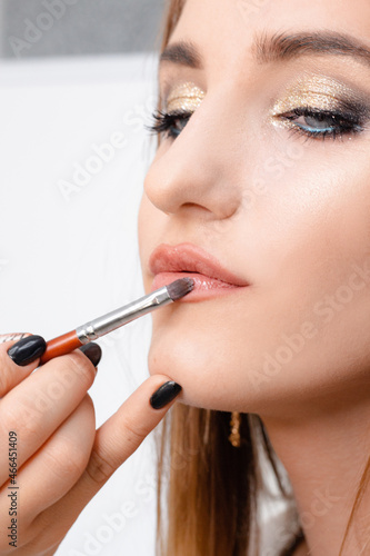 The stylist paints the lips of a beautiful girl, completes the daytime makeup in the beauty salon. Beautiful young model with bright makeup, pink lips. Real life Makeup and Cosmetology concept