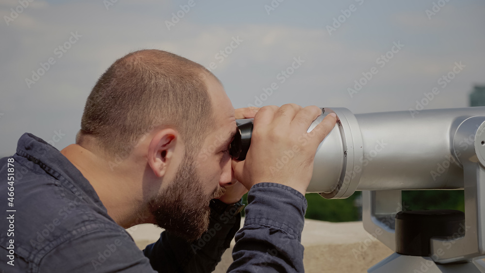 Close up of caucasian man looking through telescope lens at panoramic view of city from observation point on building roof. Young person using binoculars for outdoor panorama sightseeing
