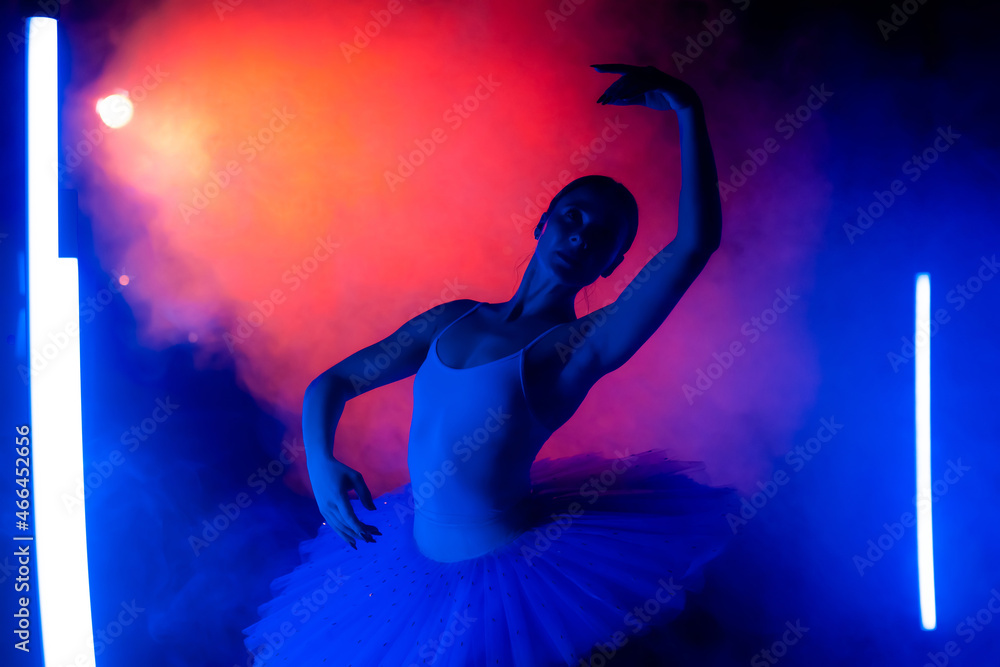 Graceful ballerina in tutu dress dancing with hands, color neon light with smoke. Woman with long dark nails and airy skirt. Studio shot. Art concept.