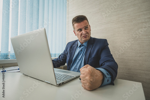 Angry man hits table with his fist. Concept of anger. angry businessman in a jacket slams his fist on table in anger looks away. boss is dissatisfied with the work of employees. fury photo