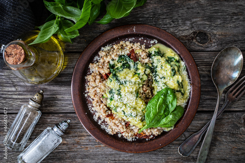 Boiled white buckwheat groats, sun dried tomatoes, parmesan and spinach served on wooden table 