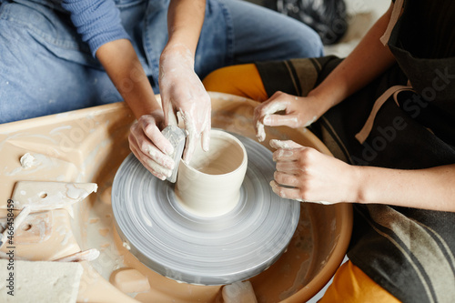 Close up of two young women working on pottery wheel together in handmade ceramics workshop, copy space