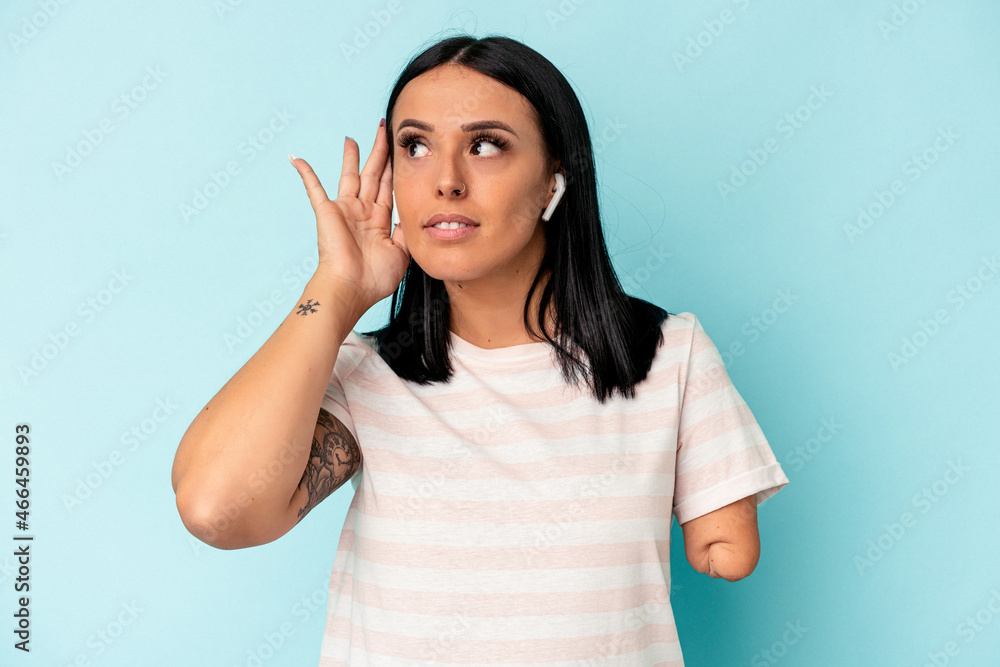 Fototapeta premium Young caucasian woman with one arm listening to music with wireless headphones isolated on blue background trying to listening a gossip.