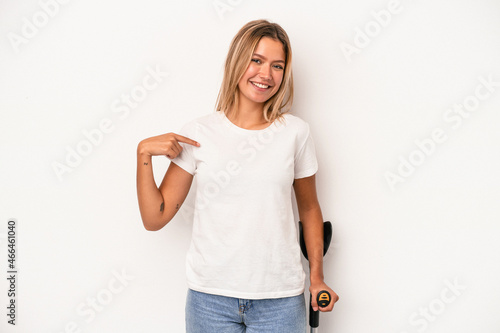 Young caucasian woman holding crutch isolated on white background person pointing by hand to a shirt copy space, proud and confident photo