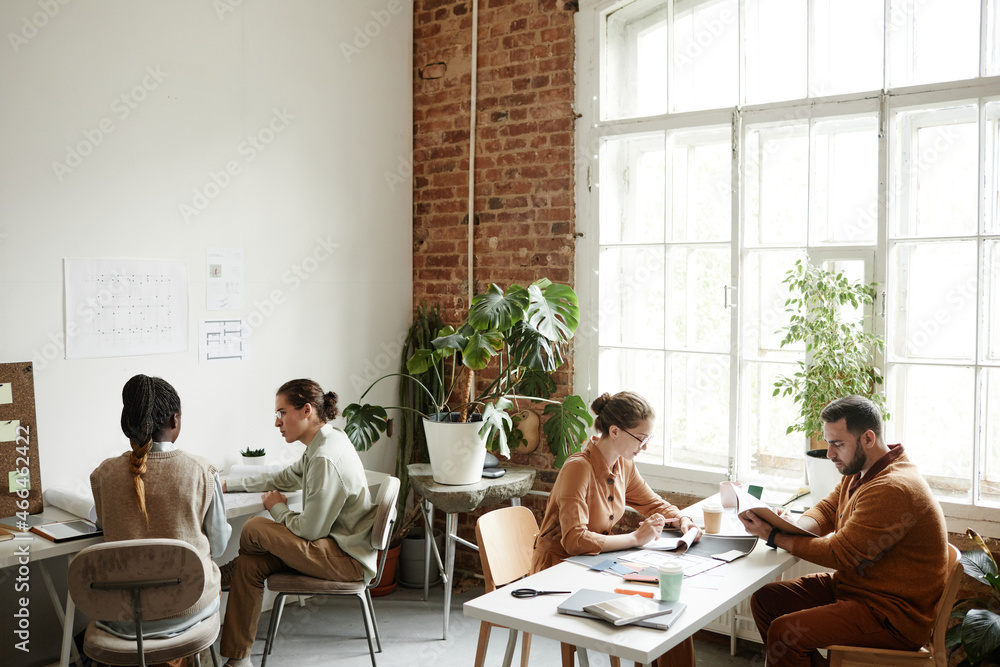 Obraz premium Wide angle portrait of diverse creative team working in modern studio lit by sunlight, copy space