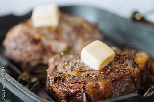 cooking sumptuous steaks in a grill pan with butter spreading over the steak seasoned with ground pepper and salt with rosemary sprigs