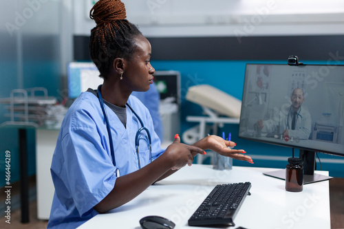 African american asisstant discussing healthcare treatment with remote therapist doctor during online videocall meeting conference working in hospital office. Telemedicine call on computer screen photo