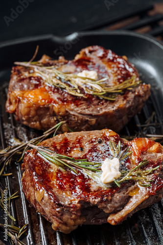 cooking sumptuous steaks in a grill pan with butter spreading over the steak seasoned with ground pepper and salt with rosemary sprigs